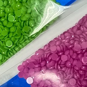 Close-up of two bags of colorful round diamond painting drills, green and purple, on a white surface.