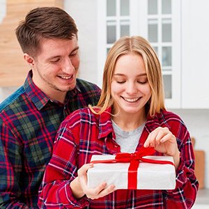 Smiling couple in plaid shirts, woman opening a white gift box with red ribbon