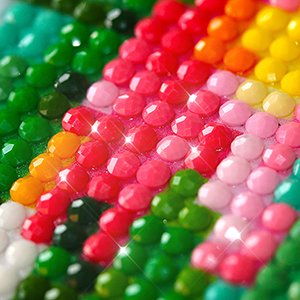 Close-up of a diamond painting kit showing rows of colorful round rhinestones in pink, red, green, orange, and yellow, sparkling under light.
