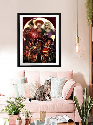 Framed Halloween diamond painting of witches and pumpkins hanging above a pink sofa with a cat.