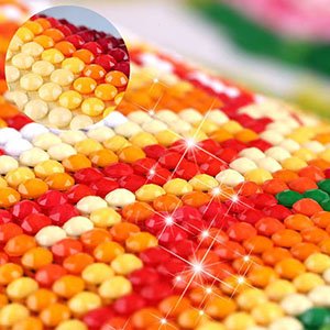 Close-up of a 5D diamond painting kit showing rows of colorful rhinestones in shades of red, orange, and yellow, with a magnified inset.