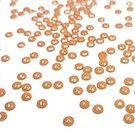 Scattered copper-colored beads on a white surface, close-up shot with shallow depth of field.
