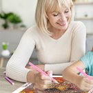 Woman and child smiling while doing a squirrel diamond painting kit at a table