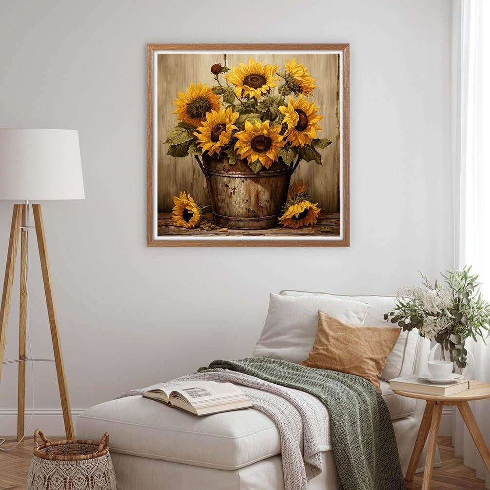 Framed diamond painting of sunflowers in a rustic bucket on a wooden surface, displayed in a living room setting.