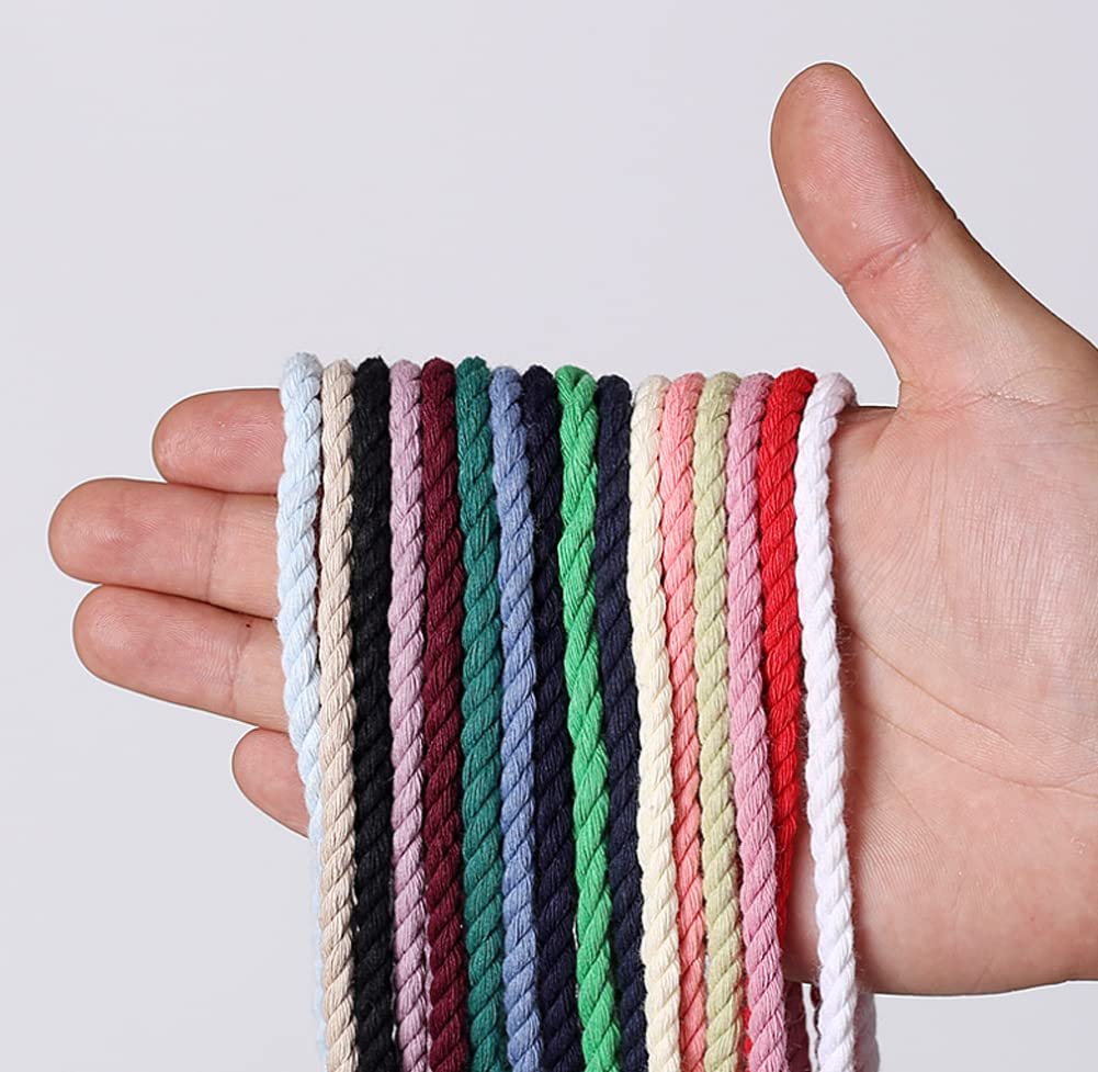 Hand holding multiple strands of colorful macrame cord against a white background