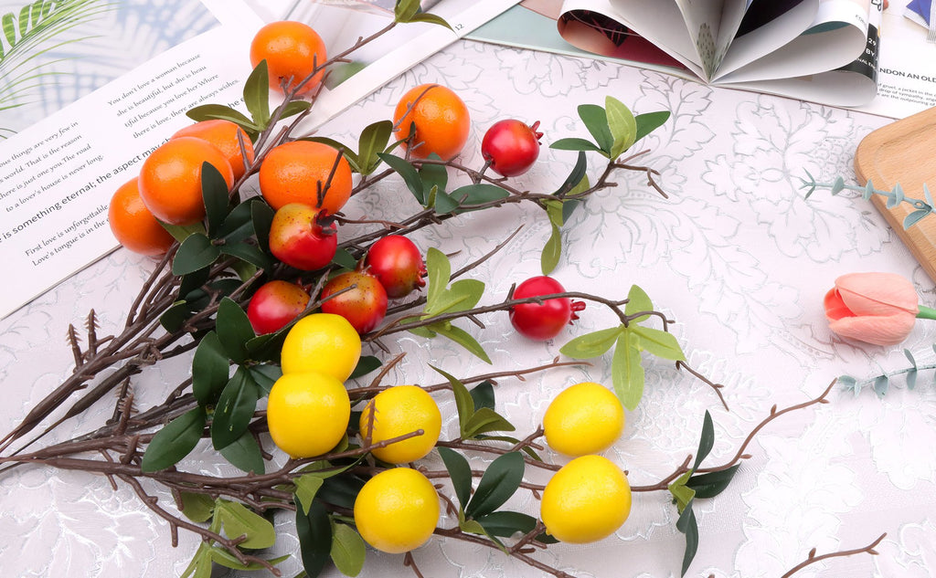 Artificial pomegranate and orange branches with silk leaves and foam fruits arranged on a textured surface with an open book.