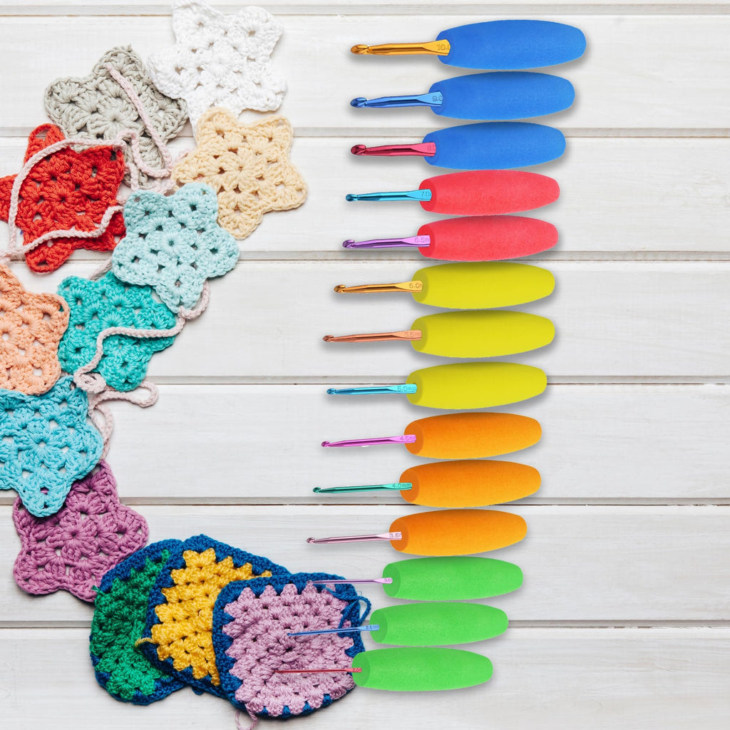 Crochet hooks with colorful ergonomic grips and various crocheted star and square motifs on a white wooden background.