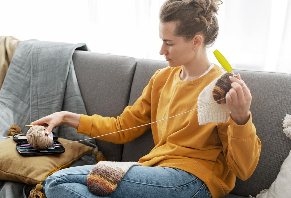 Woman crocheting on a sofa with a yarn ball and crochet hooks in a case