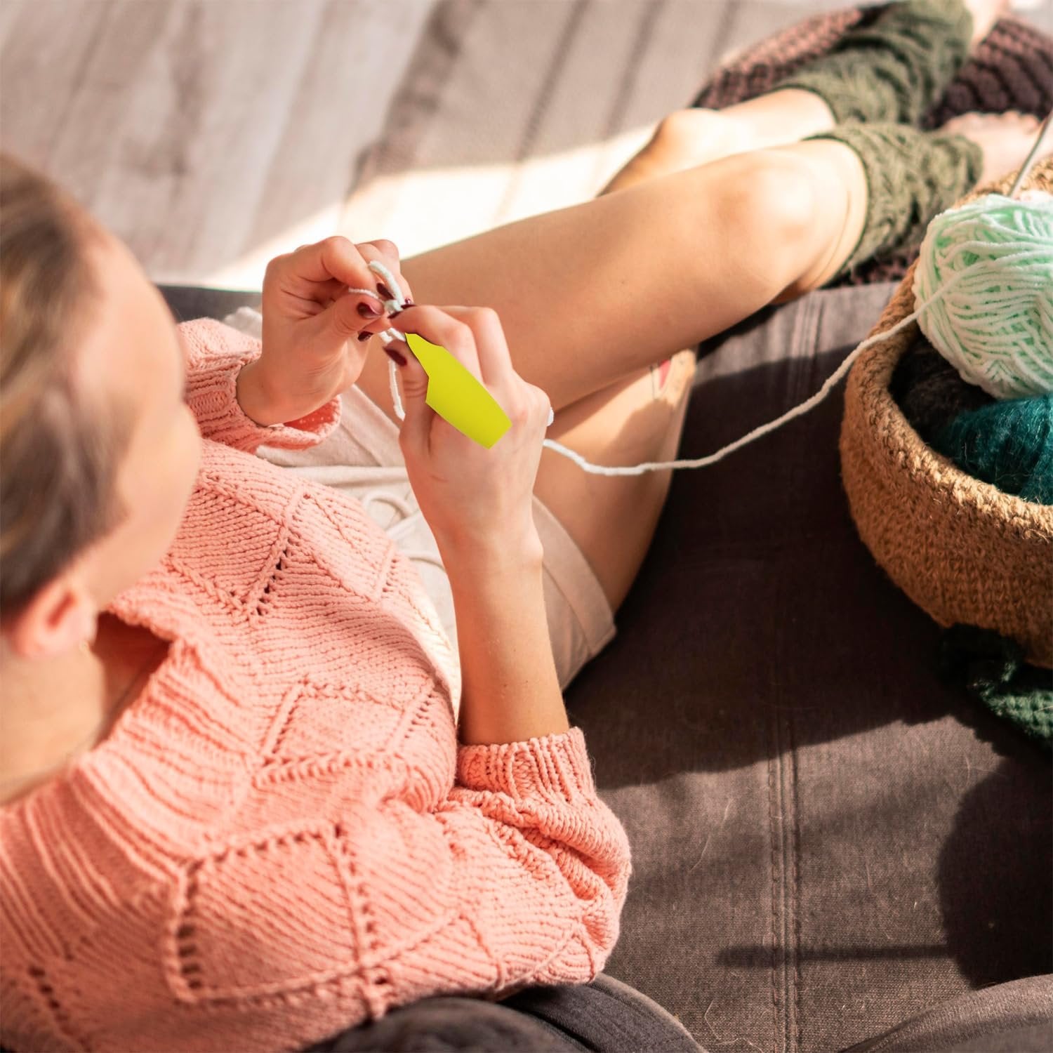 Person crocheting with yarn in a basket, wearing a pink sweater and green leg warmers.