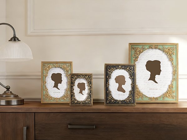 Four decorative picture frames with silhouette inserts displayed on a wooden dresser