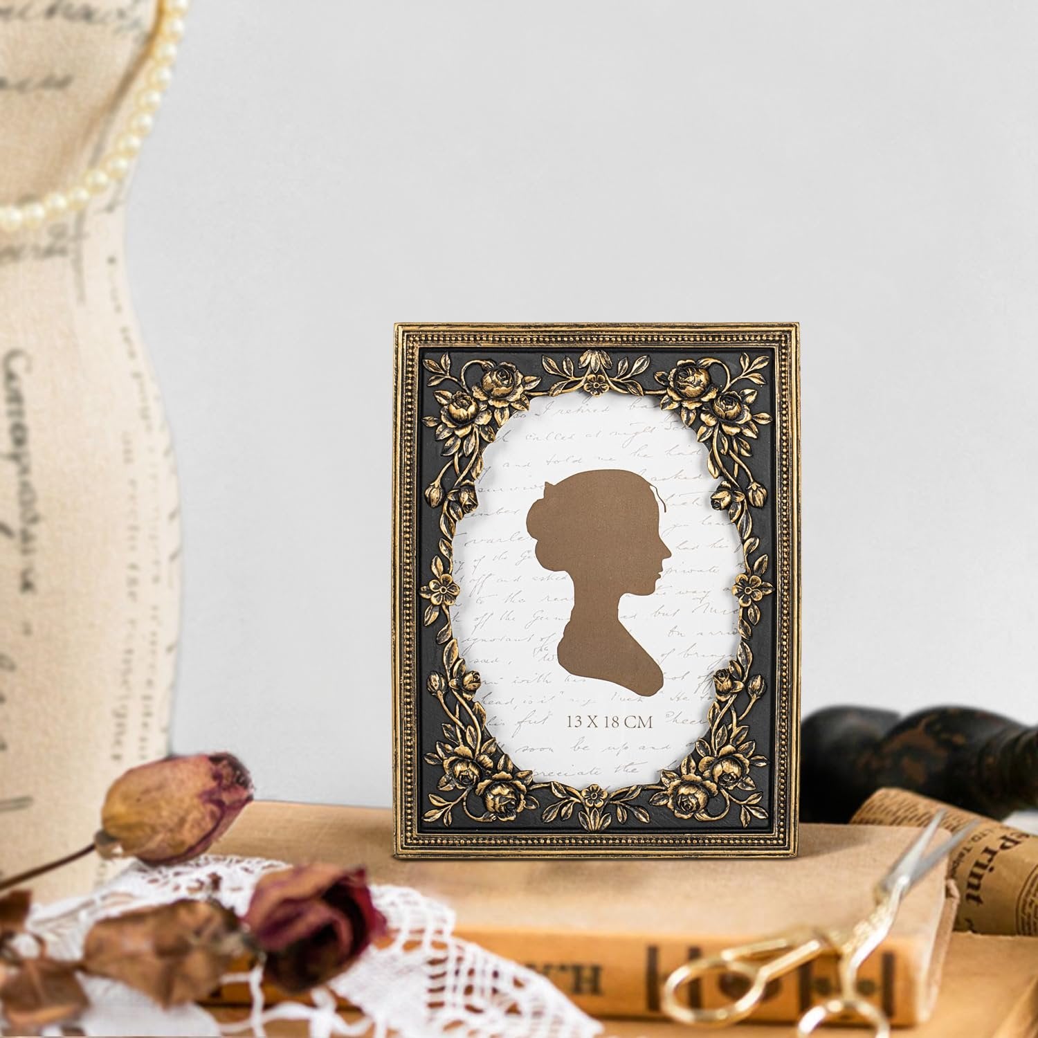 Vintage black and gold ornate picture frame with floral details, displaying a silhouette and text, set on a book.