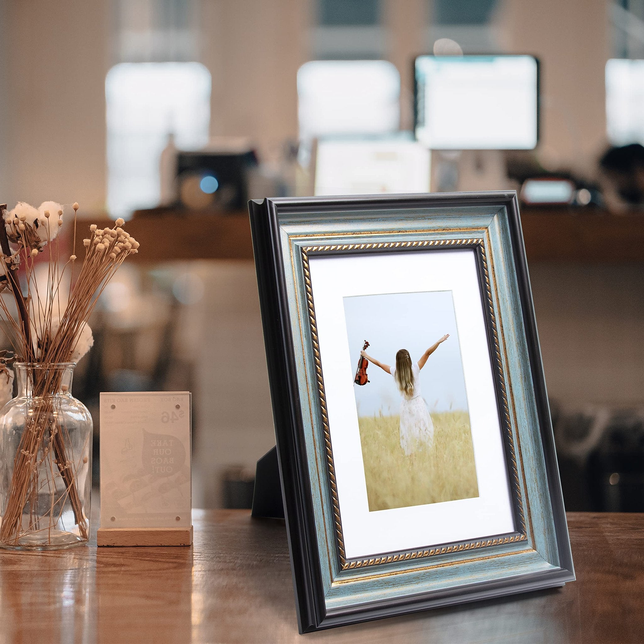 Peacock blue picture frame with gold trim displaying a photo of a woman in a field holding a violin