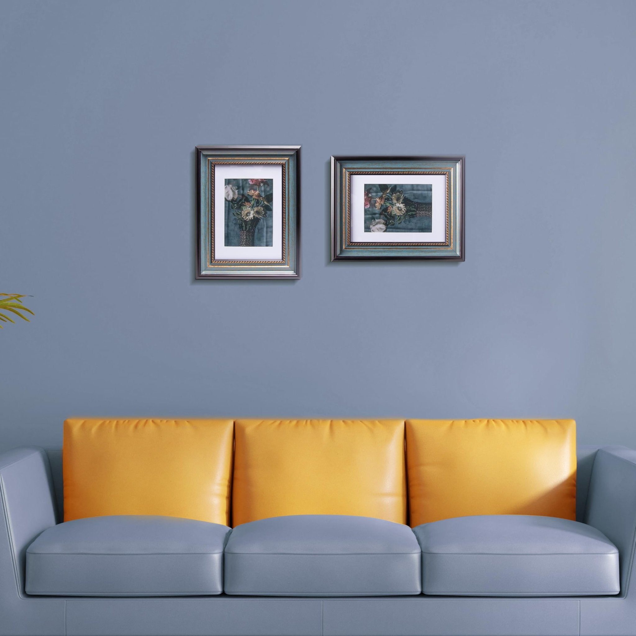 Two peacock blue picture frames with floral art displayed on a gray wall above a gray and yellow sofa.