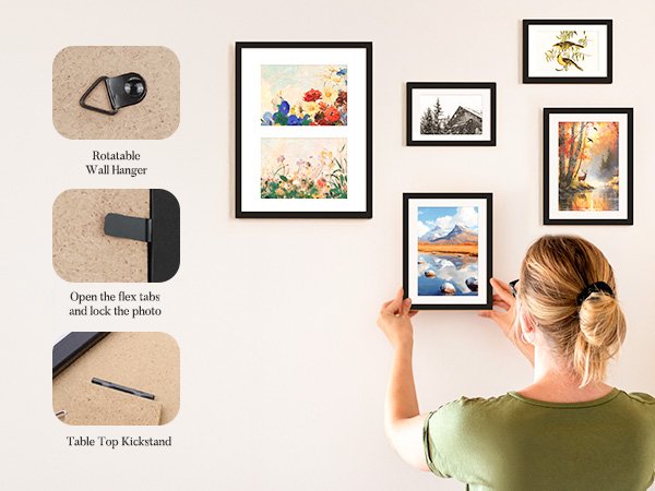 Woman hanging a black picture frame on a wall displaying a landscape painting, surrounded by other framed art.