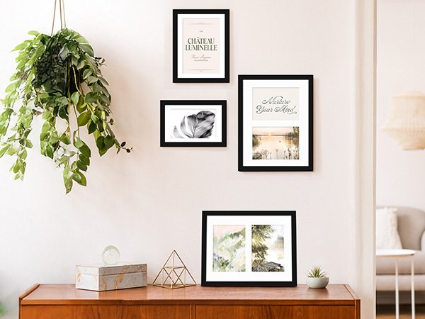 Four black picture frames arranged on a wall above a wooden dresser with decorative items.
