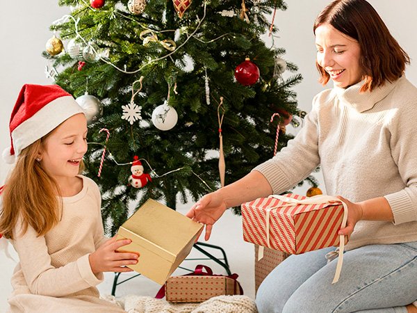 Mother and daughter exchanging Christmas gifts in front of a decorated tree