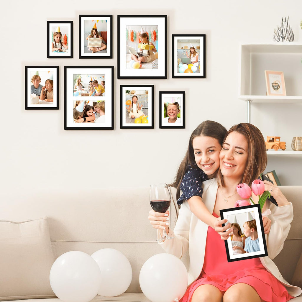 Woman and daughter holding a picture frame with children celebrating a birthday, surrounded by framed photos on a wall.