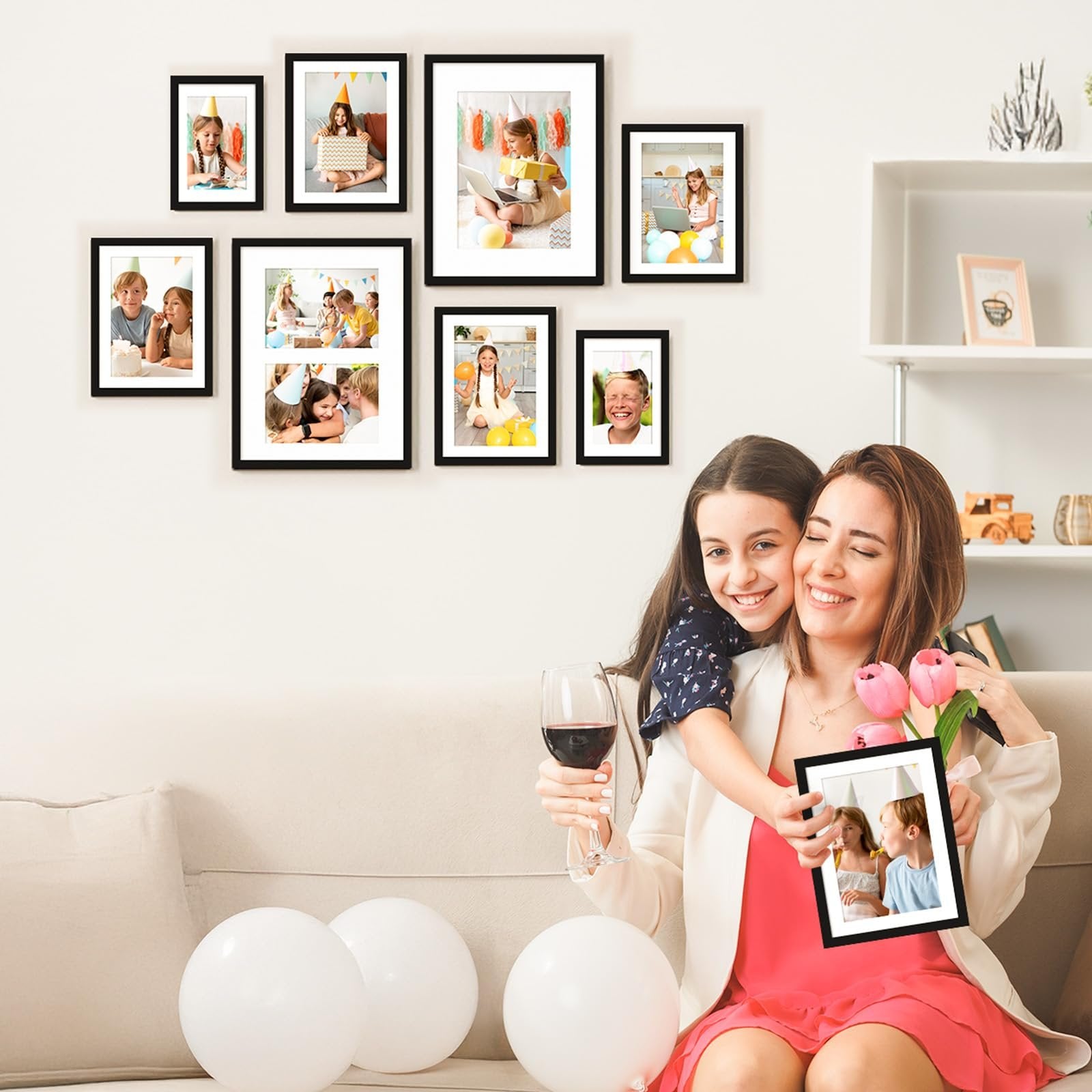 Woman and daughter holding a picture frame with children celebrating a birthday, surrounded by framed photos on a wall.