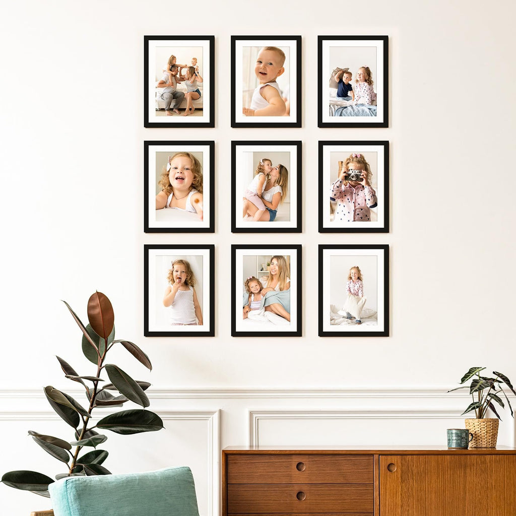 Nine framed photos of children and families displayed on a white wall above a wooden credenza.