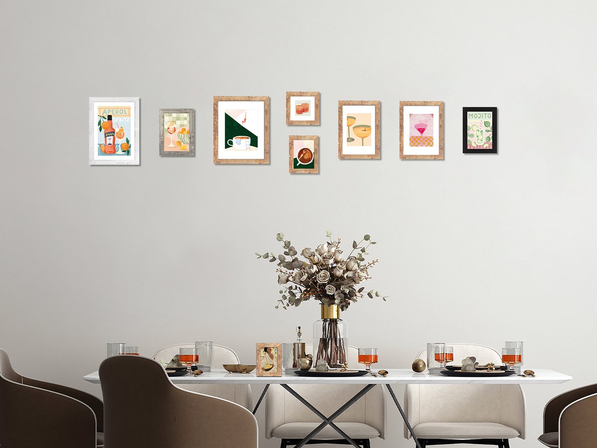 Gallery wall of eight framed prints above a dining table with a floral arrangement and place settings.