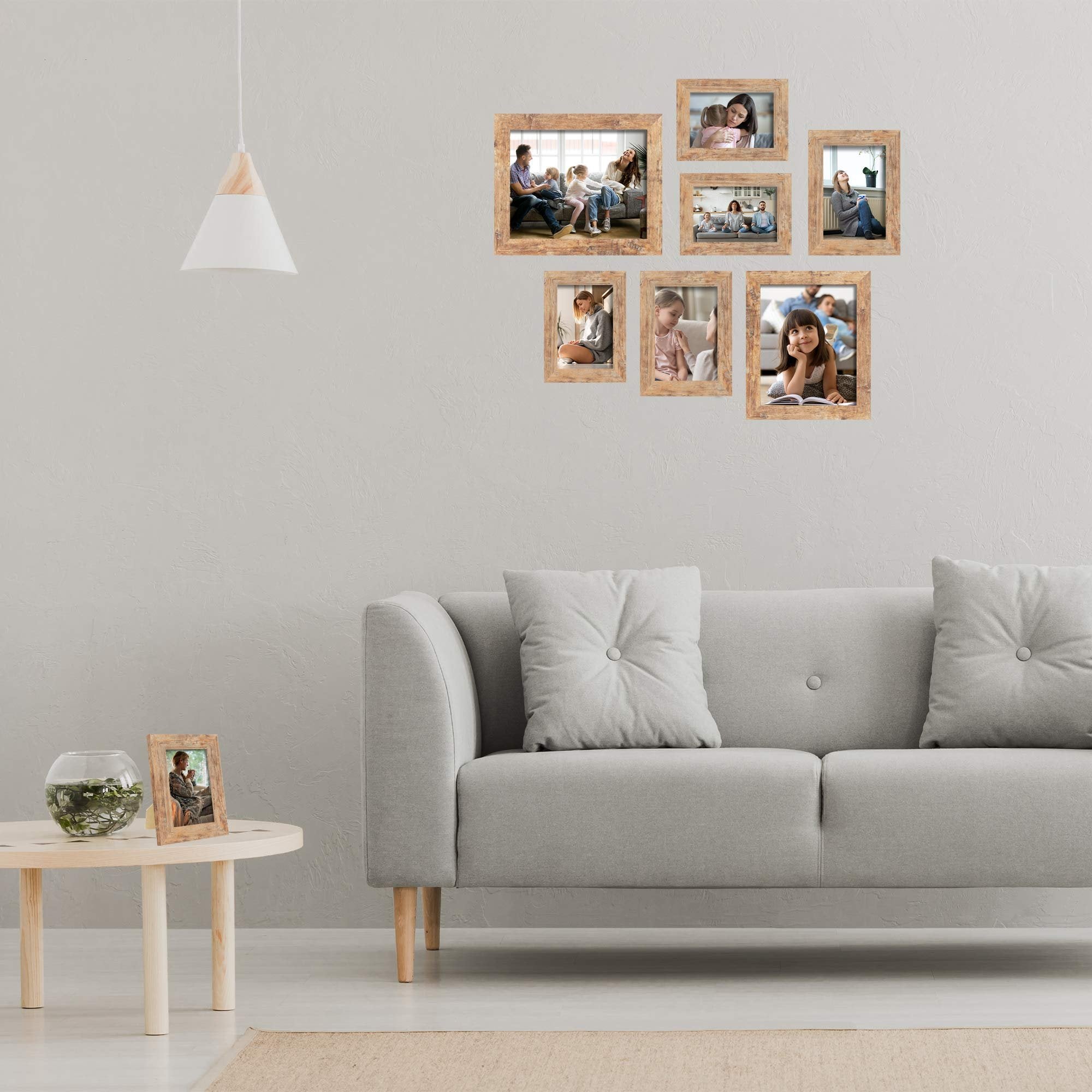 Rustic brown picture frames arranged on a wall above a grey sofa, with one frame on a side table.