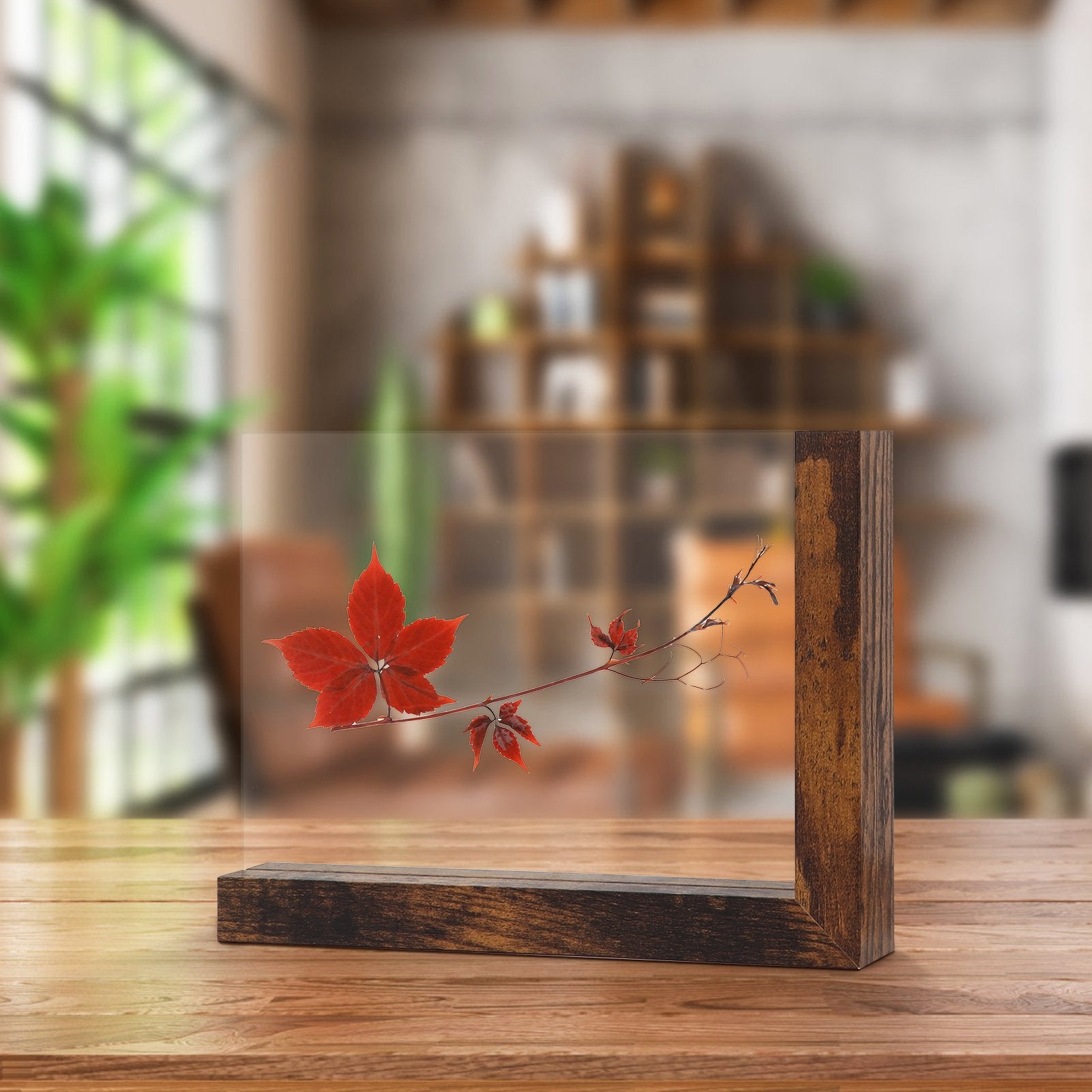 Double-sided glass picture frame with wooden base displaying a red leaf branch, set on a wooden table.