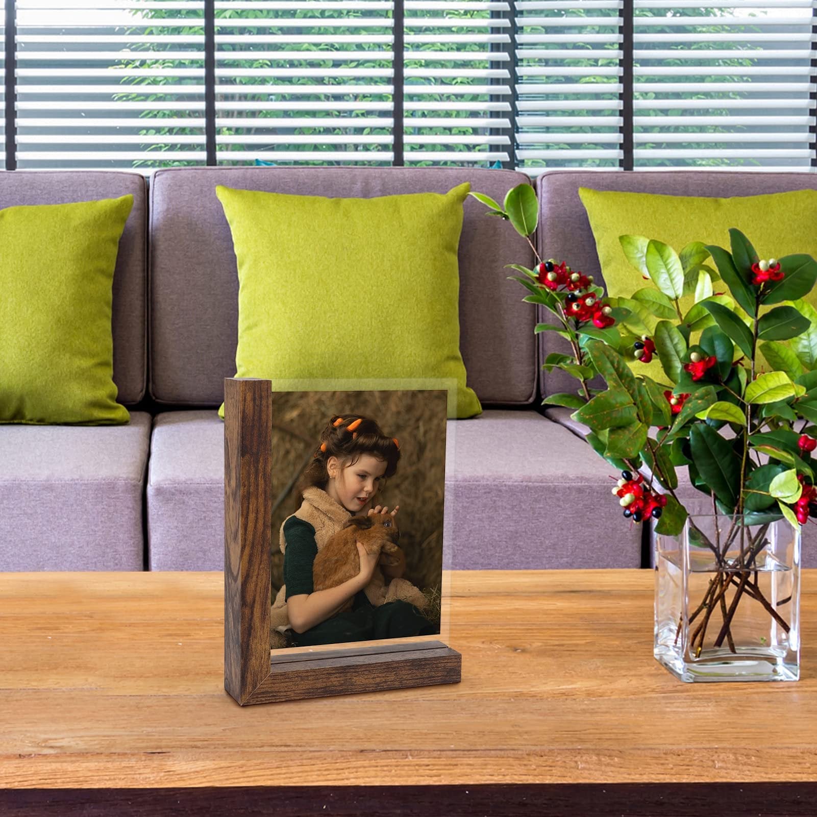 Wooden picture frame displaying a young girl holding a rabbit, on a wooden table with a sofa and plant in the background.