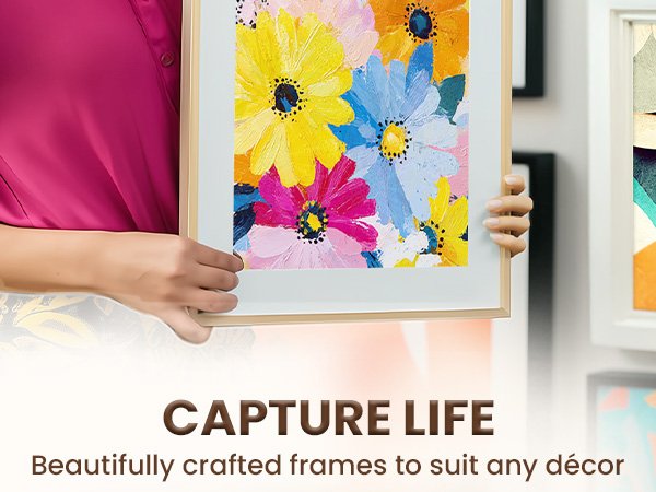 Hands holding a framed painting of colorful flowers, with other frames visible in the background.