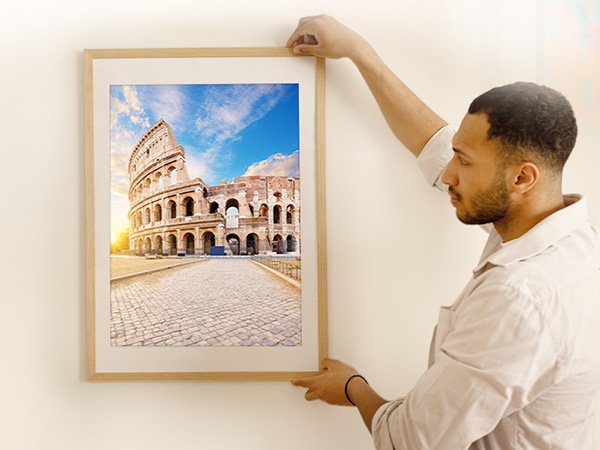 Man hanging a framed picture of the Colosseum in Rome on a white wall