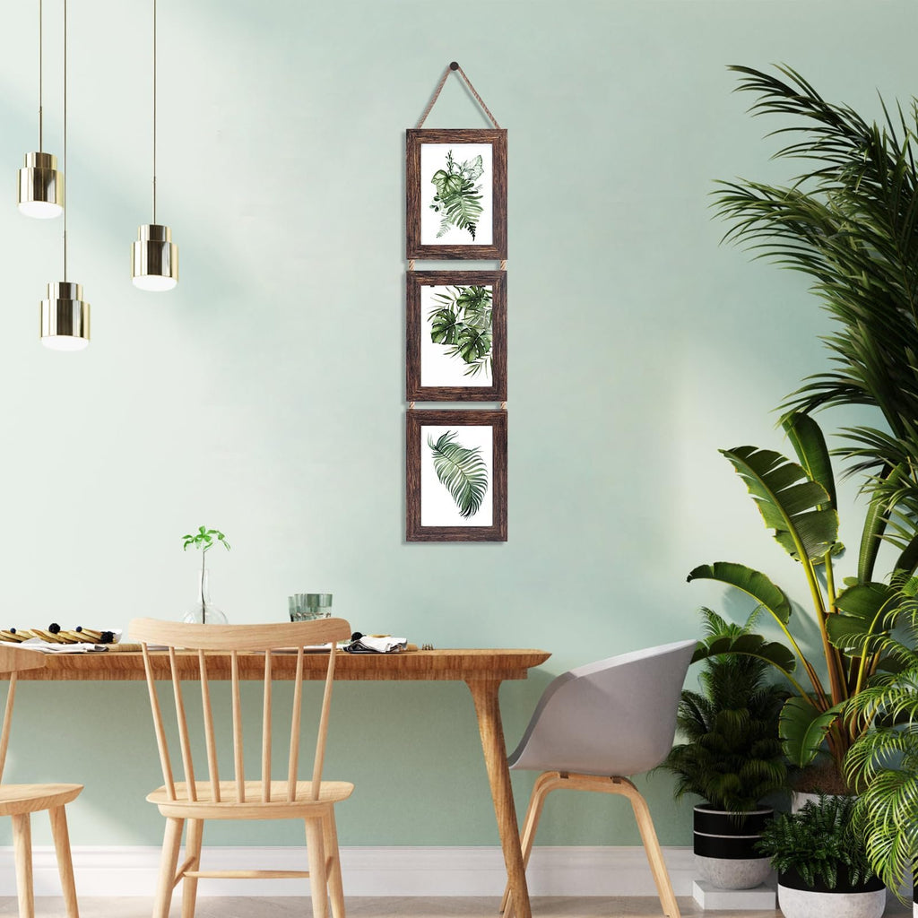 Triple vertical wall hanging picture frame with distressed brown wood finish, displaying botanical prints, hung above a wooden table.