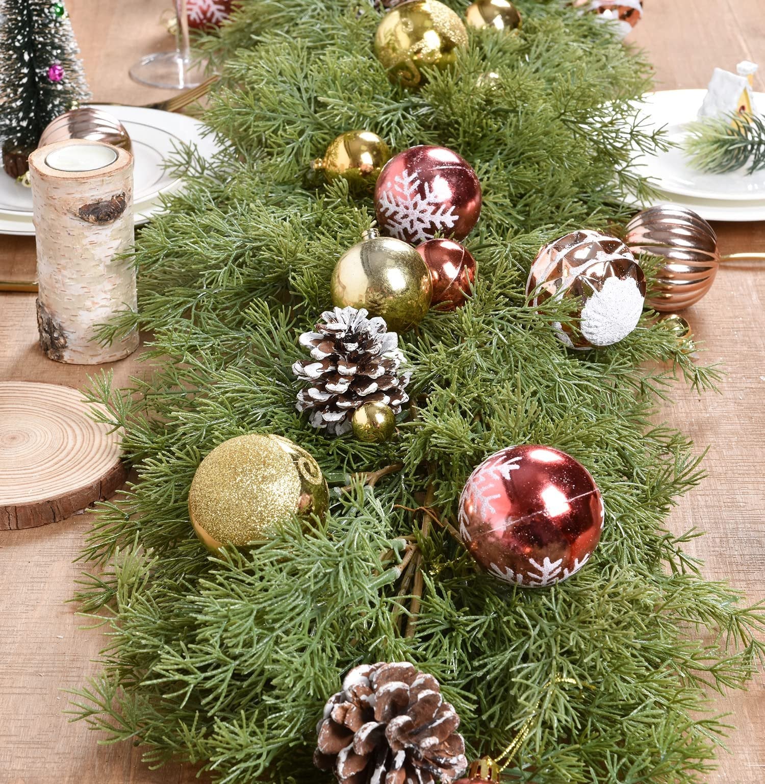 Artificial pine Christmas garland with gold and red ornaments and pine cones on a wooden table