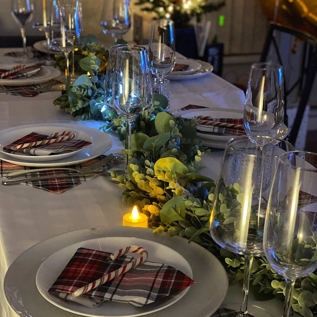Table setting with faux eucalyptus garland, plates, silverware, wine glasses, and candy canes.