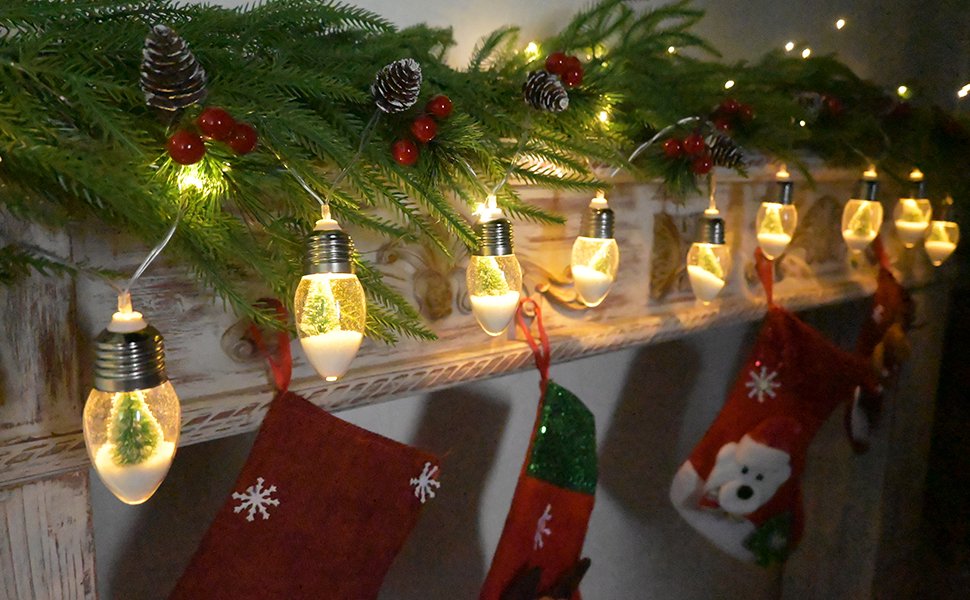 Christmas pine garland with lights and snow globe bulbs draped over a mantle with stockings