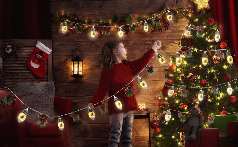 Girl decorating a Christmas tree with pine garland lights, featuring snow globe bulbs and pinecone accents.