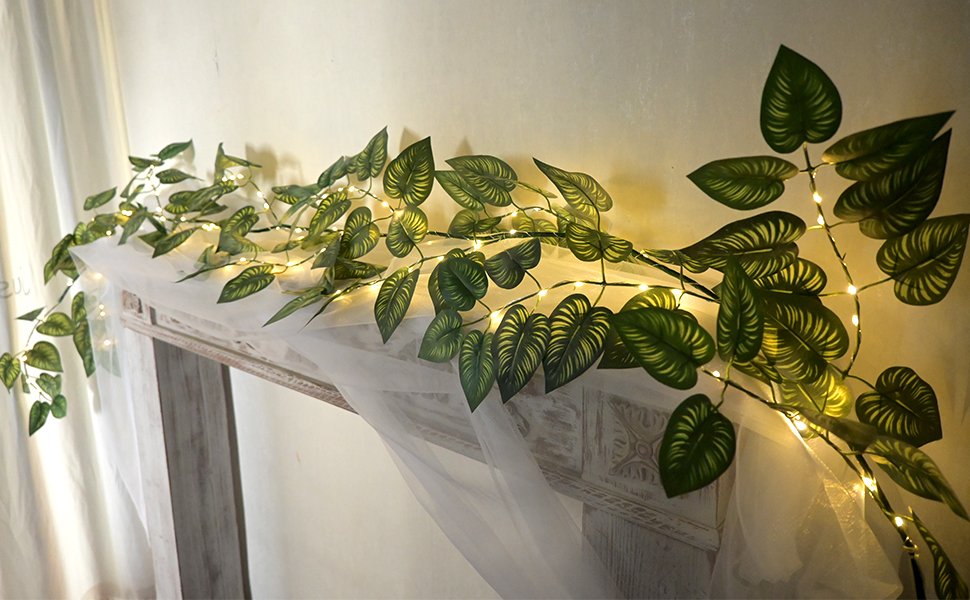 Green vine garland with 96 LED lights draped over a mantelpiece with sheer white fabric.