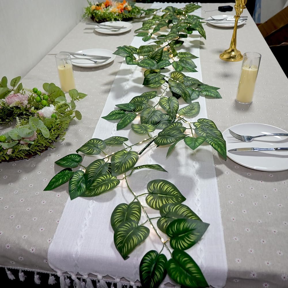Green vine garland with LED lights draped across a table setting with plates, cutlery, and candles.