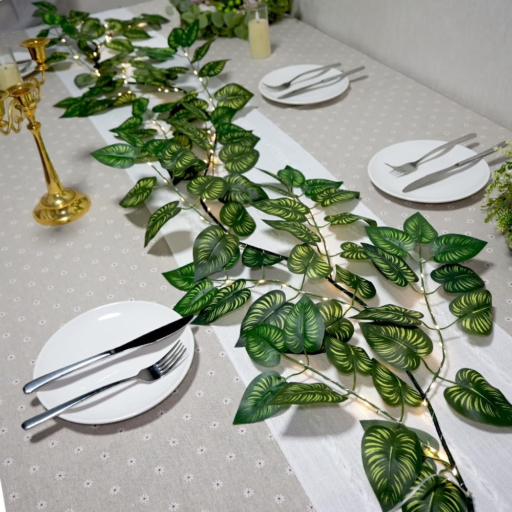 Green vine garland with LED lights draped across a table setting with plates and cutlery.