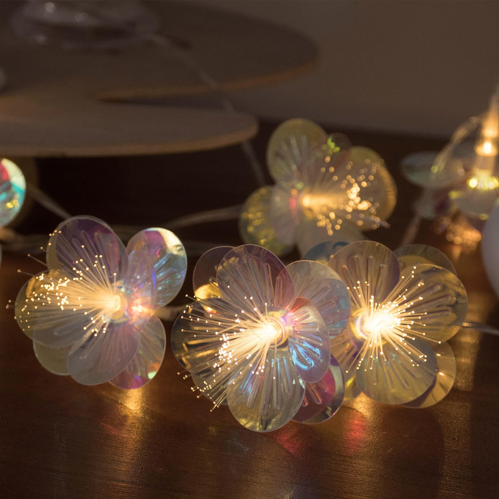 Close-up of fiber optic flower string lights with warm white LEDs on a wooden surface.