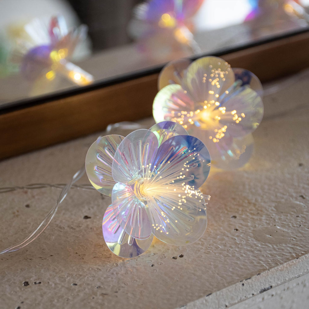 Close-up of iridescent fiber optic flower string lights with warm white LEDs, reflected in a mirror.
