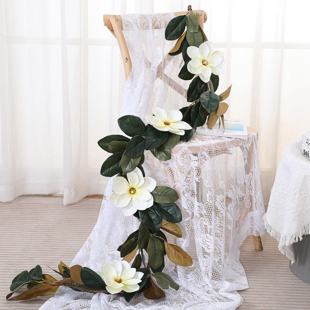 Artificial magnolia garland with white flowers and green leaves draped over a chair and table with lace coverings.