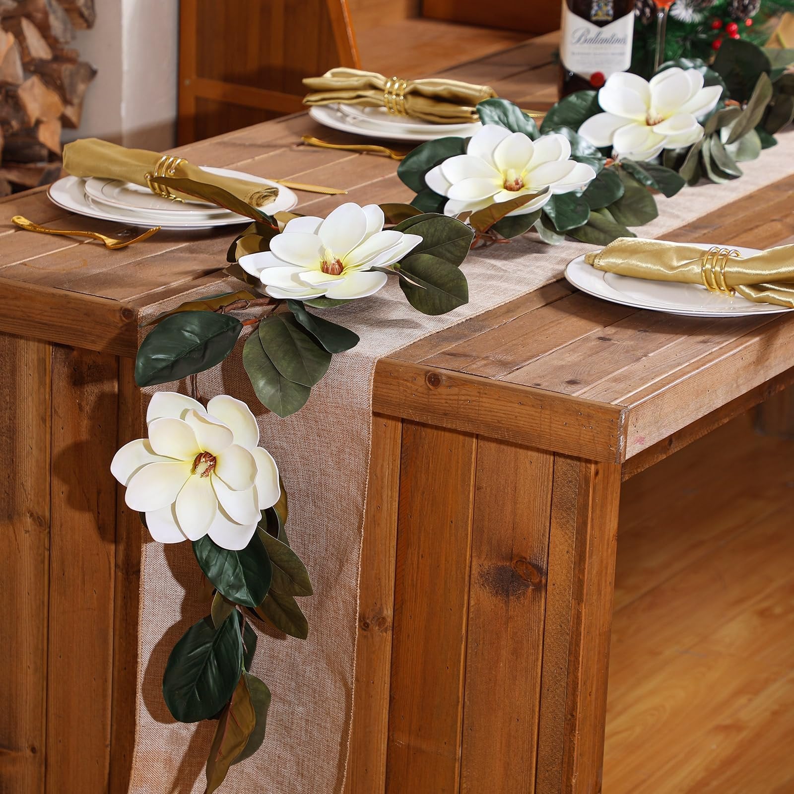 Artificial magnolia garland with white flowers and green leaves draped across a wooden table with place settings.