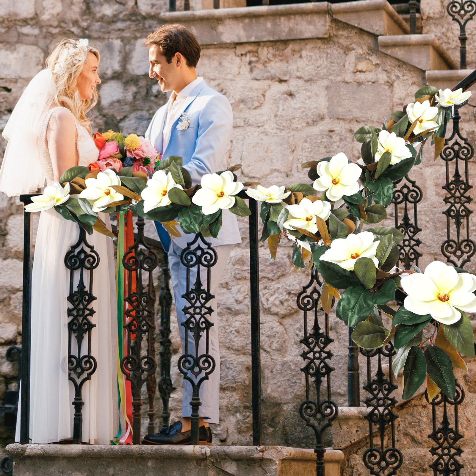 Bride and groom on stairs with artificial magnolia garland draped on railing