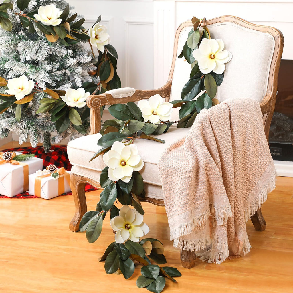 Artificial magnolia garland with white flowers and green leaves draped over a chair next to a Christmas tree.