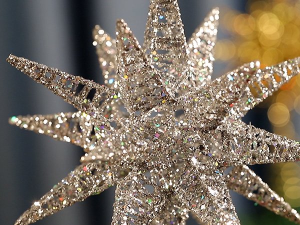 Close-up of a silver glitter starburst Christmas tree topper with intricate cutouts, soft focus background.