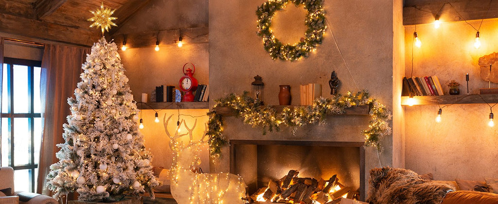 Festive Christmas living room scene with a flocked tree topped with a star, a fireplace with garland and wreath, and a lighted reindeer decoration.