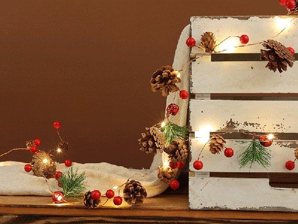 Christmas garland with pinecones, red berries, and LED lights draped over a white wooden crate.