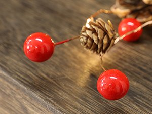 Close-up of a prelit Christmas garland with pinecones, red berries, and warm white LED lights on a wooden surface.