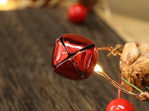 Close-up of a red metallic bell ornament on a Christmas garland with pinecones and LED lights.
