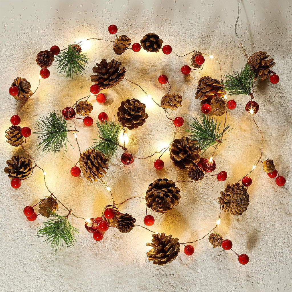 Christmas garland with pinecones, red berries, and warm white LED lights arranged on a textured surface.