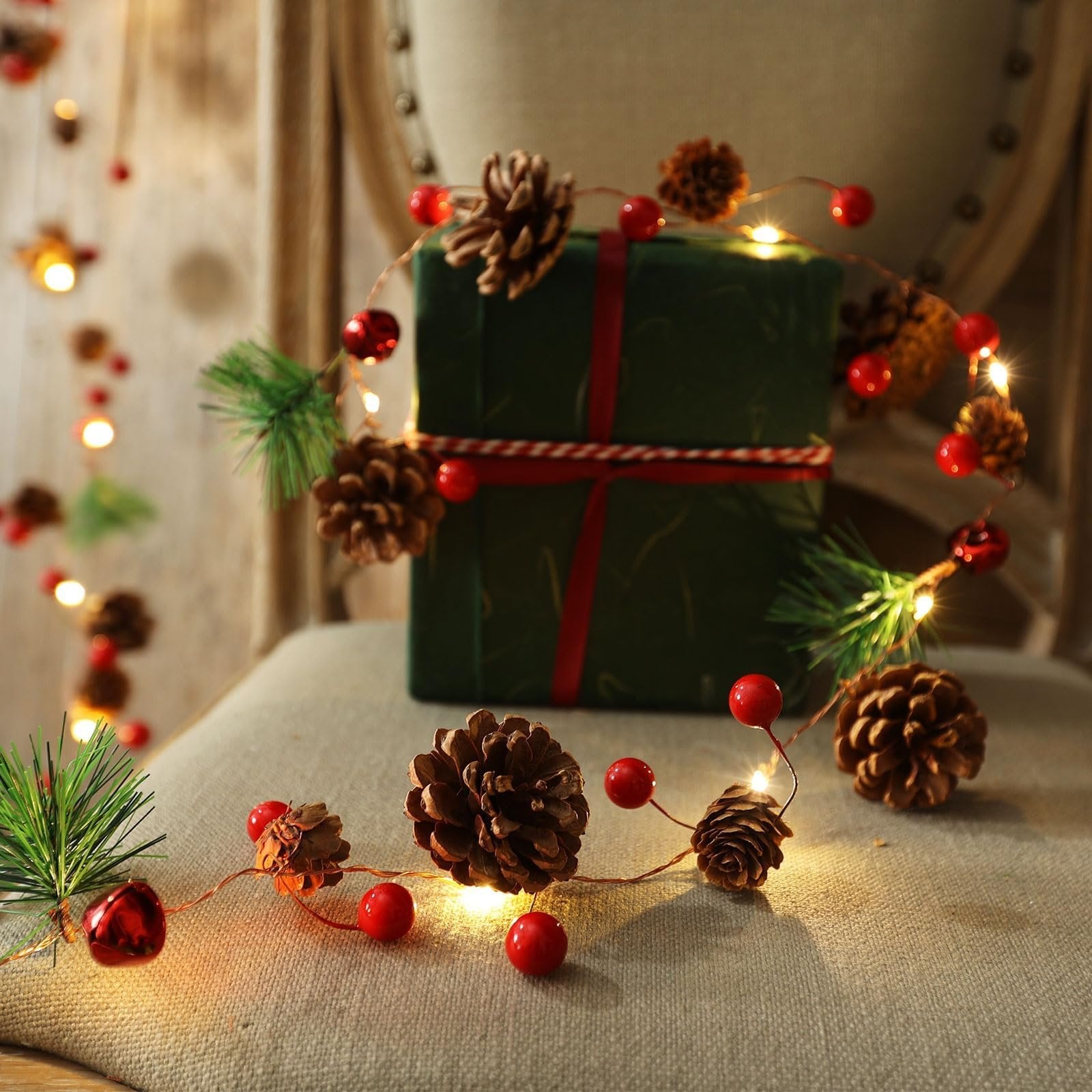 Christmas garland with pinecones, red berries, bells, and warm white LED lights draped around a gift.